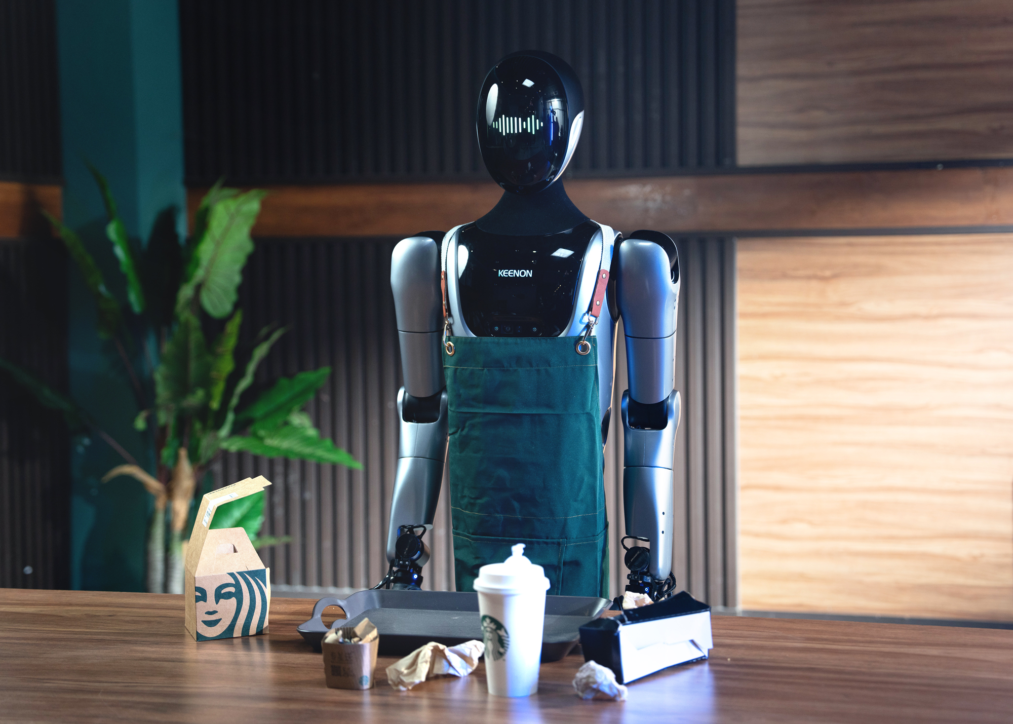 KEENON XMAN-R1 humanoid service robot working as a barista behind a café counter wearing an apron