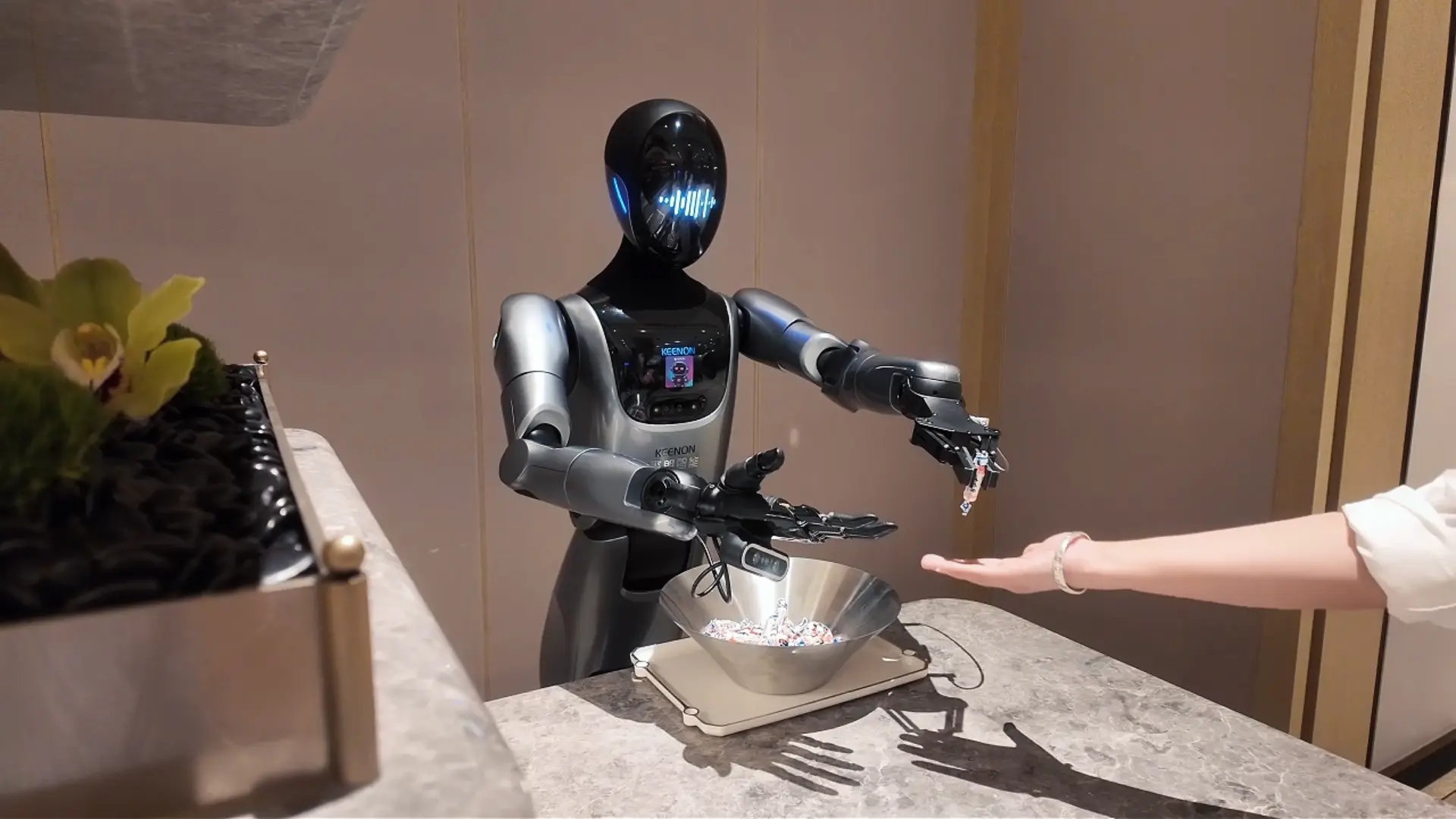 KEENON XMAN-R1 humanoid service robot passing an item to a guest's hand at a counter