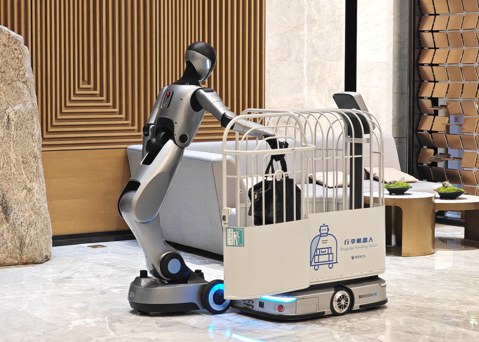 KEENON XMAN-R1 humanoid service robot loading a guest's bag into a luggage cart in a hotel lobby